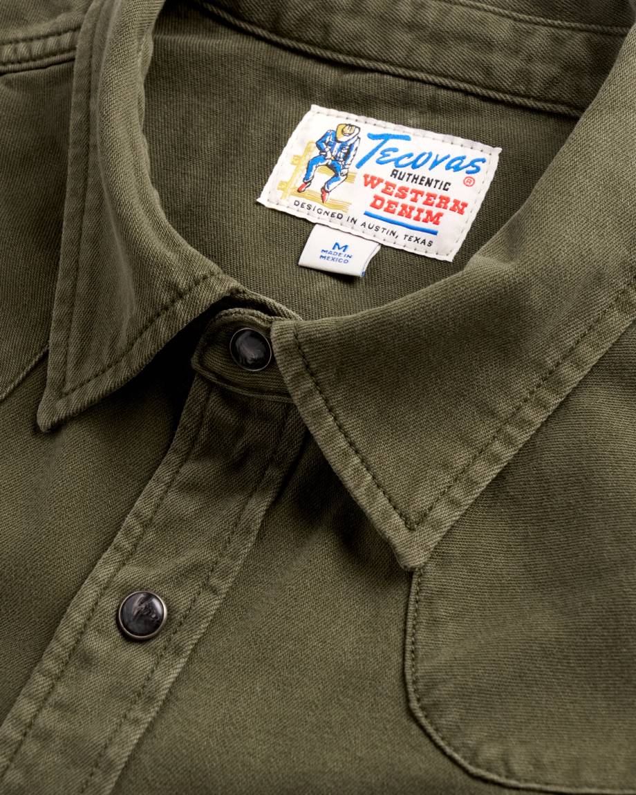 Close-up of an olive green denim shirt collar with a "Tecovas" brand label and a size M tag made in Mexico.