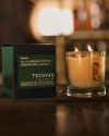 A lit candle with a boot design beside a dark green box labeled "Tecovas Ranger Station" on a wooden surface.