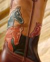 Close-up of a brown leather boot with embroidered horse head designs in green, orange, and burgundy.