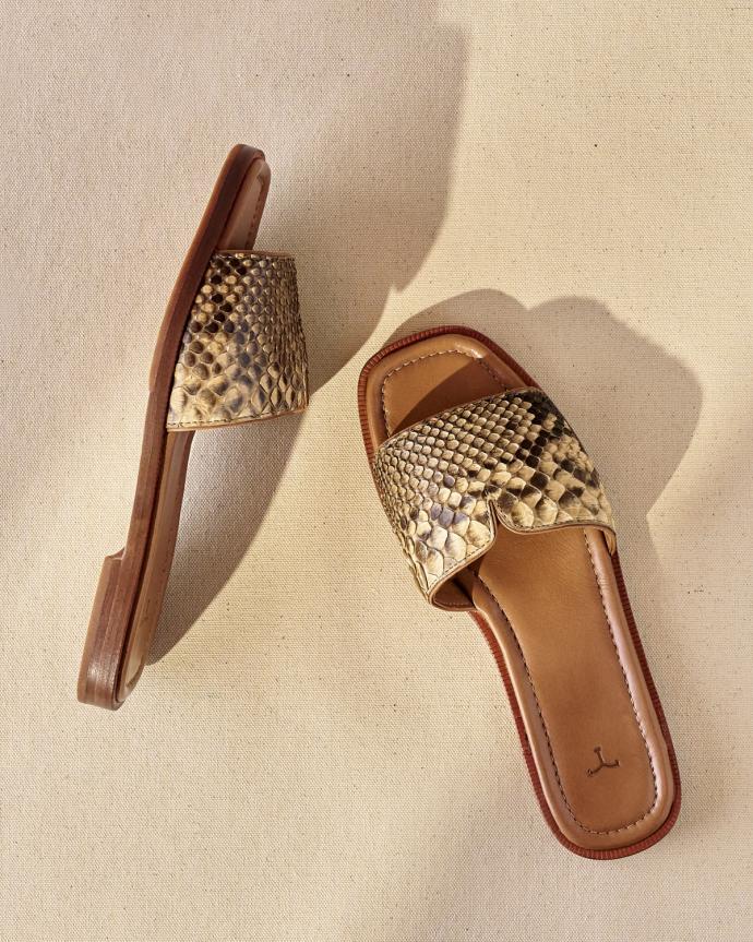 Two snake-patterned sandals with brown soles are shown on a beige background.