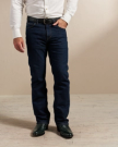 A person wearing dark blue jeans, a white long-sleeved shirt, a black belt, and black shoes stands in front of a beige wall. Only the lower half of their body is visible.