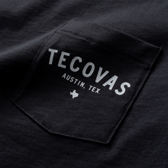 Close-up of a black fabric showing a pocket with "TECOVAS AUSTIN, TEX" printed in white text, accompanied by a small Texas silhouette.