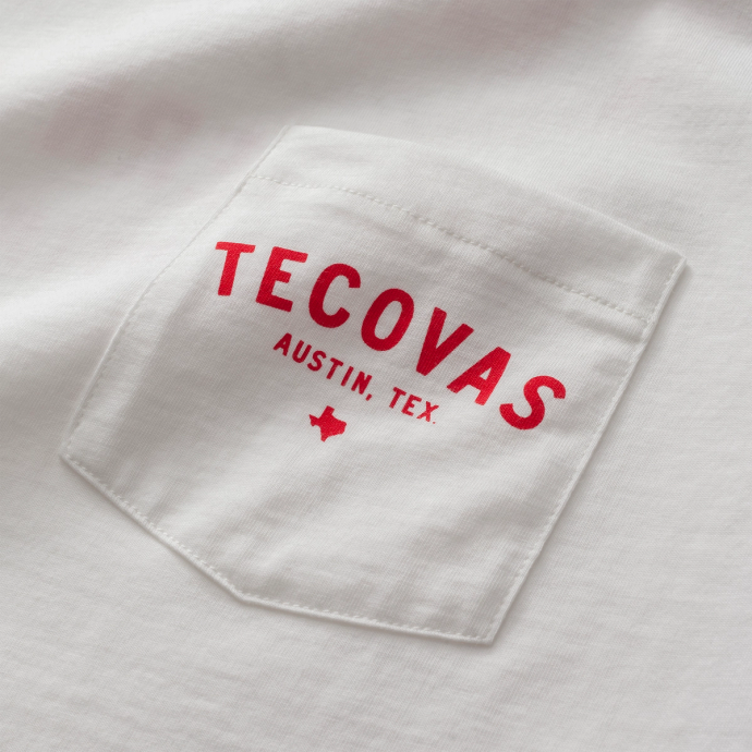 White fabric with a pocket featuring the red text "TECOVAS AUSTIN, TEX." with a small Texas state outline underneath.