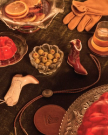 A tabletop with a bowl of olives, a drink, red gelatin, orange slices in punch, leather gloves, two miniature cowboy boots, a bolo tie, and a leather coaster.