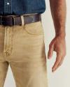 A person wearing light tan jeans, a dark brown belt, and a blue denim shirt, with their right arm hanging relaxed at their side.