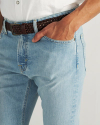 Close-up of a person wearing light blue jeans, a white shirt, a brown woven belt, and resting a hand in their front pocket.