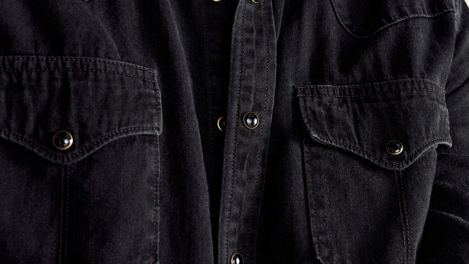Close-up of a black denim shirt showing buttons and two chest pockets with flaps.