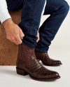 Brown cowboy boots with intricate patterns on the shaft and pointed toes. One boot is upright facing forward, the other is angled sideways.