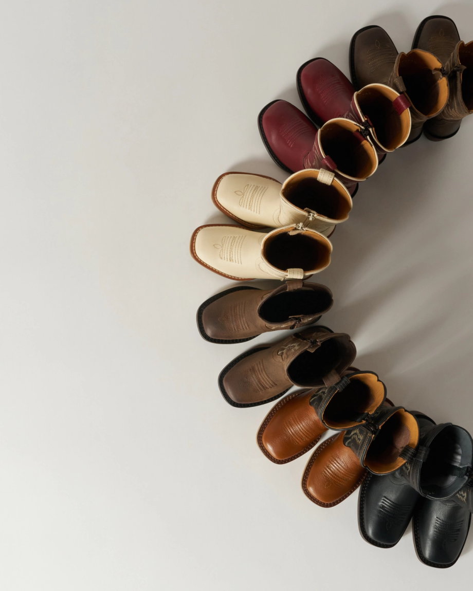 A circle of cowboy boots in various colors, including black, brown, beige, and burgundy, arranged on a light background.