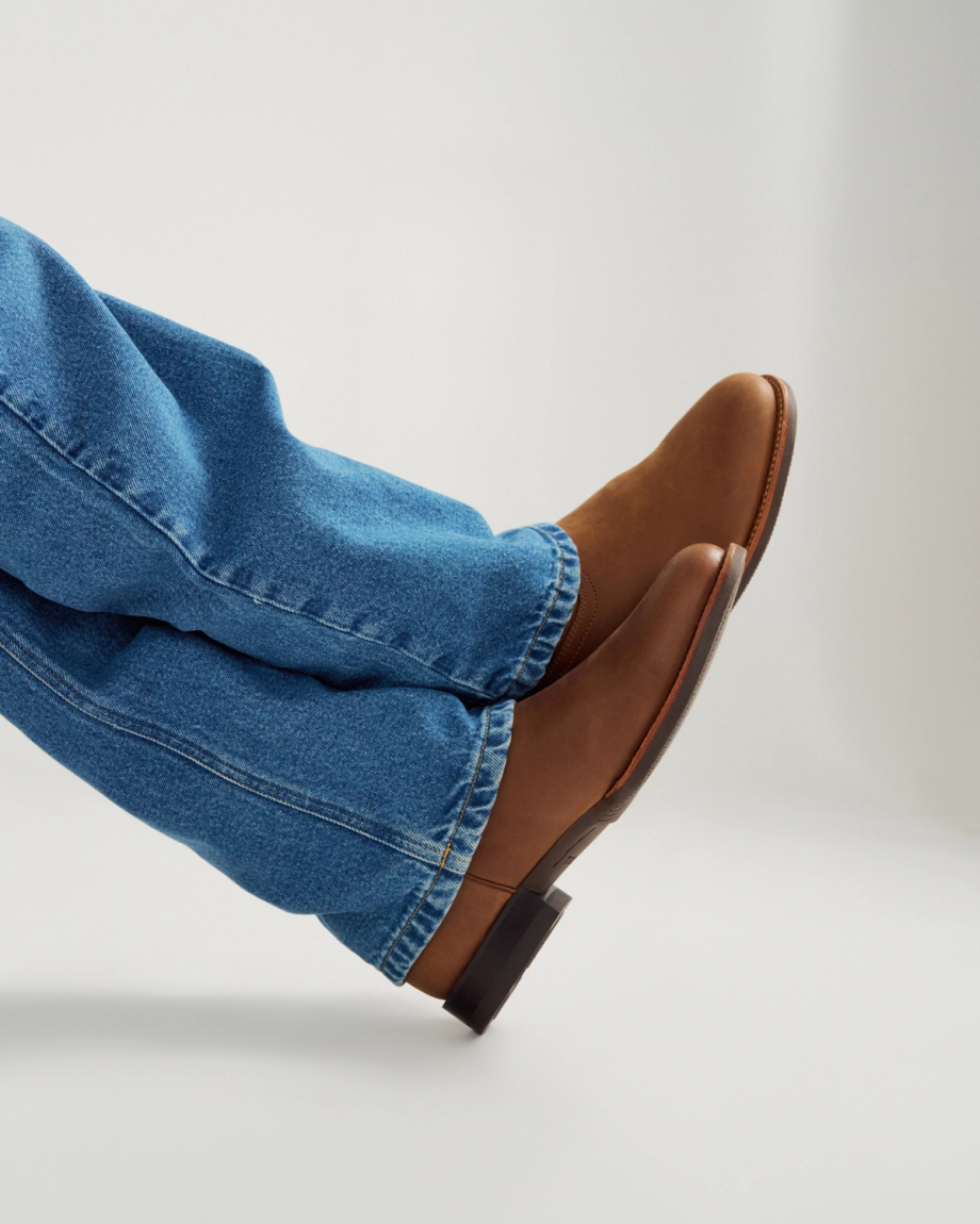 The Glen in Khaki Cowhide. A person wearing blue jeans and brown leather Khaki Cowhide shoes with a low heel, photographed against a plain background.