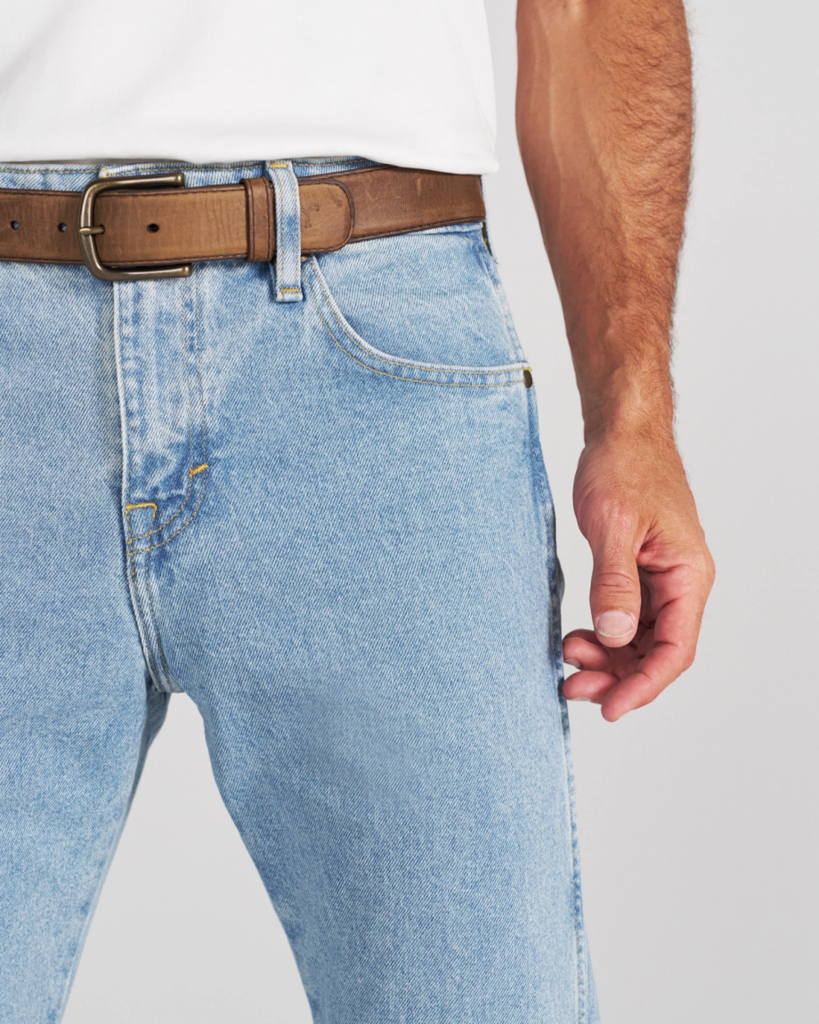 A person wearing light blue jeans with a brown leather belt and a white t-shirt.