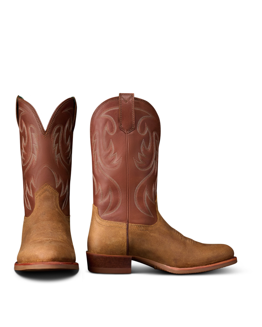 The Buck in Copper Cowhide. Pair of brown western cowboy boots, named The Buck Cowhide, with a light brown foot and darker brown shaft featuring decorative stitching, shown from the front and side on a white background.