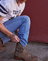 Person wearing a Texas t-shirt and blue jeans adjusting their brown cowboy boot.