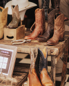 Several pairs of cowboy boots are displayed on a rustic wooden table, with a hat and horseshoes also visible.