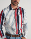 Man wearing a button-up shirt with vertical white, blue, and red stripes, two chest pockets, blue jeans, and a brown belt. Upper body shown; face is partially out of frame.