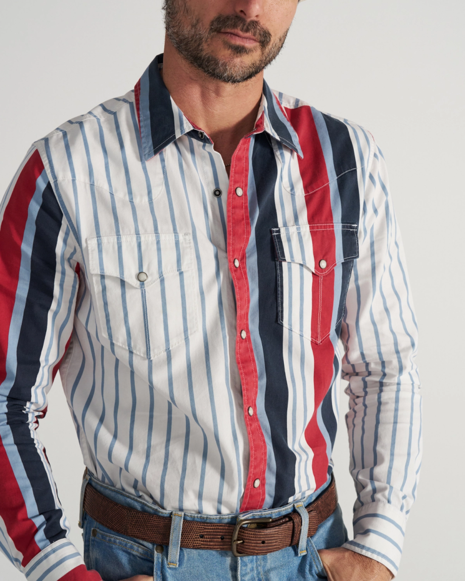 Man wearing a button-up shirt with vertical white, blue, and red stripes, two chest pockets, blue jeans, and a brown belt. Upper body shown; face is partially out of frame.