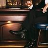 Man in suit and alligator boots drinking a cocktail at a fancy bar