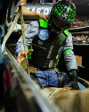 A rodeo rider, wearing protective gear with a helmet, prepares to ride a bull in a pen. The rider is holding onto a rope while sitting on the bull.