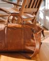 The Bartlett Large Weekender in Cognac resting on a wooden table
