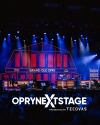 A microphone stands on a branded pedestal on stage at the Grand Ole Opry, with the venue's name illuminated in the background.