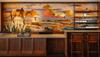 A mural of a cowboy and horse in a western landscape decorates the wall behind a wooden counter and shelves in a rustic-style café with two bar stools.