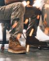 Person sitting on a chair wearing work boots and pants, surrounded by flying sparks from metalwork.