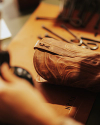 A brown leather bag lies on a workbench surrounded by metal tools, indicating a leather crafting or repair process.