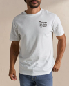 A man wearing a white T-shirt with a small logo on the left chest that reads "Tecovas Quality Western Goods." He is also wearing blue jeans and has a tattoo on his left arm.