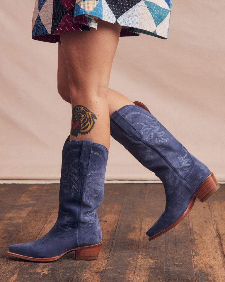 A woman wearing an indigo suede cowgirl boot.