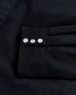 Close-up of a black fabric sleeve with three white buttons aligned in a row.