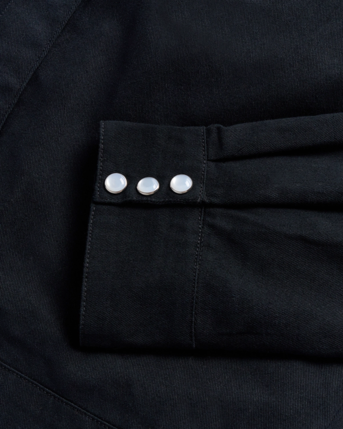 Close-up of a black fabric sleeve with three white buttons aligned in a row.