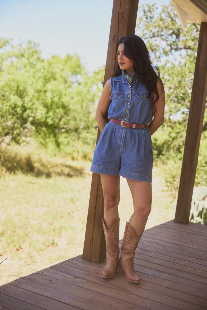 Woman in a denim romper and boots standing on a porch