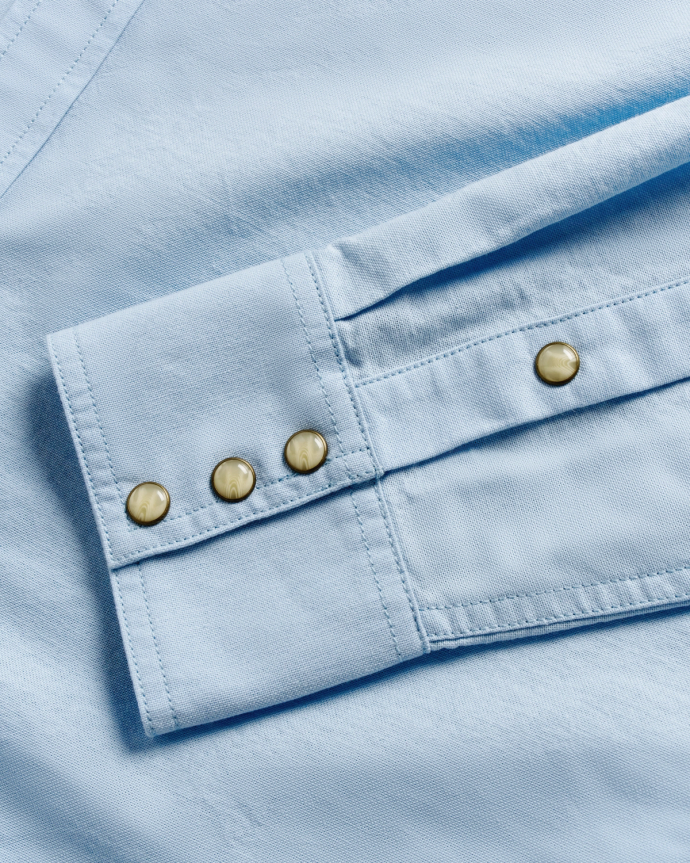 Close-up of a light blue fabric with a cuff featuring three metallic buttons lined vertically.