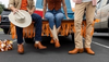Three people sitting on a tailgate showing off their Tecovas boots and clothes.