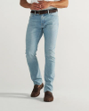 A person wearing light blue jeans, a black belt, and brown loafers stands against a plain white background.
