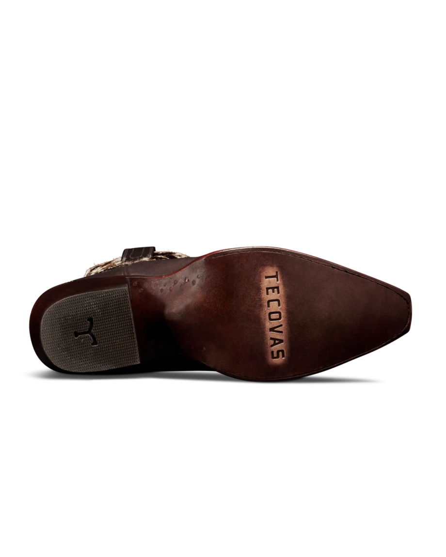 The Sadie in Hair on Hide Hair on Hide / Cowhide. The underside of a brown Hair on Hide cowboy boot with "Tecovas" stamped on the leather sole and a rubber grip near the heel.