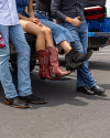 Three people sitting on the back of a truck, showcasing their western-style boots: one pair of bright red boots, one pair of black fringe boots, and one pair of plain black boots.