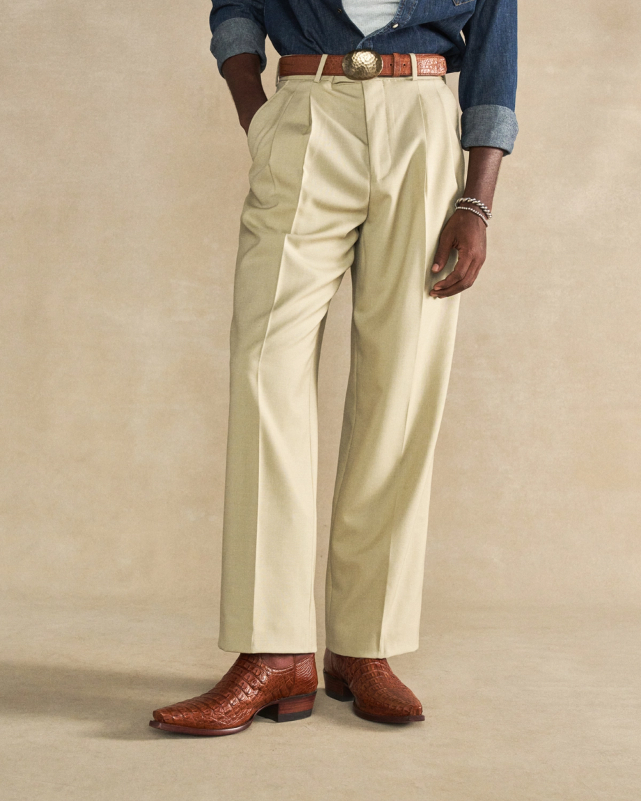 The Garrett in Pecan Hornback Caiman. A person wearing beige pleated dress pants, a brown pecan belt with a large buckle, brown Hornback Caiman cowboy boots, and a denim shirt with sleeves rolled up.