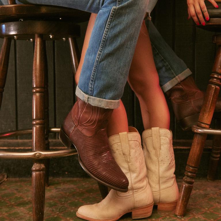 a couple hugging at a bar from the legs down wearing cowboy boots