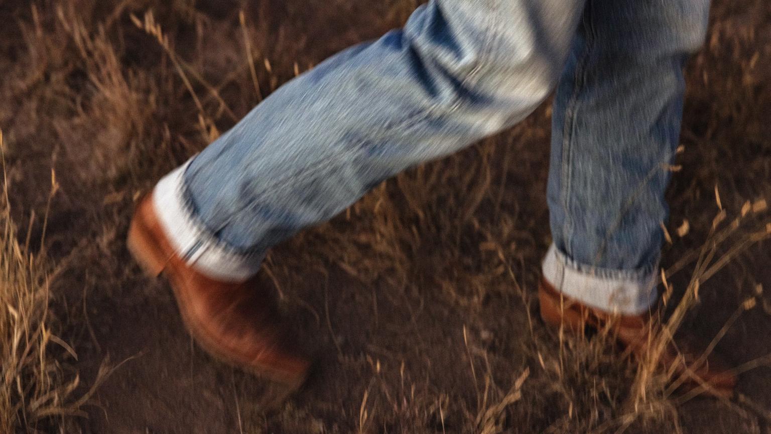 Closeup of mans jeans and boots while he walks through a field