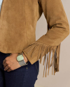 Close-up of a person wearing a tan suede jacket with fringes on the sleeve, blue jeans, and a silver bracelet with a large pastel green stone.