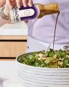 Person pouring salad dressing from a "SideDish" bottle onto a large bowl of salad.