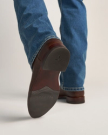 The Earl in Tobacco Bison. Close-up of a person wearing blue jeans and brown cowboy boots, with the sole of one boot visible showing the "TECO VAS" branding—a classic look that pairs well with The Earl Bison collection.