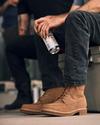 Two people sitting, with a focus on one person wearing brown boots and holding a beverage can.