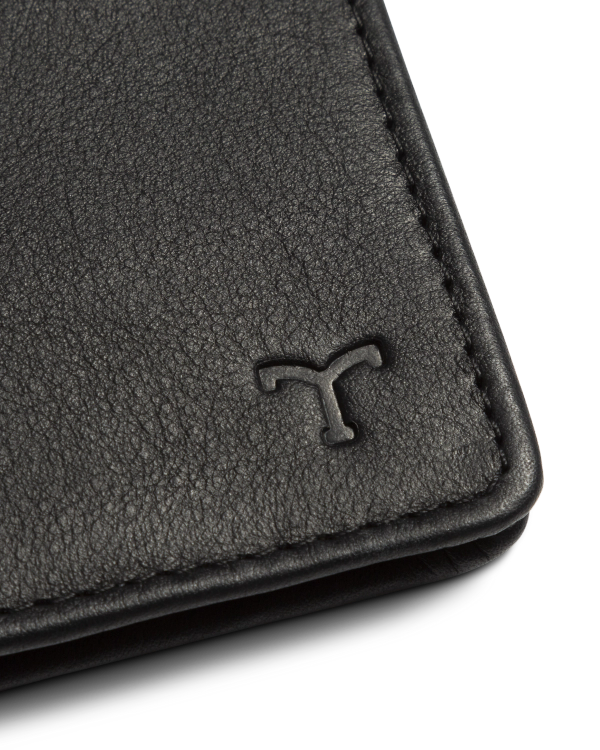 Close-up of a black leather wallet corner with a T logo embossed on the surface.