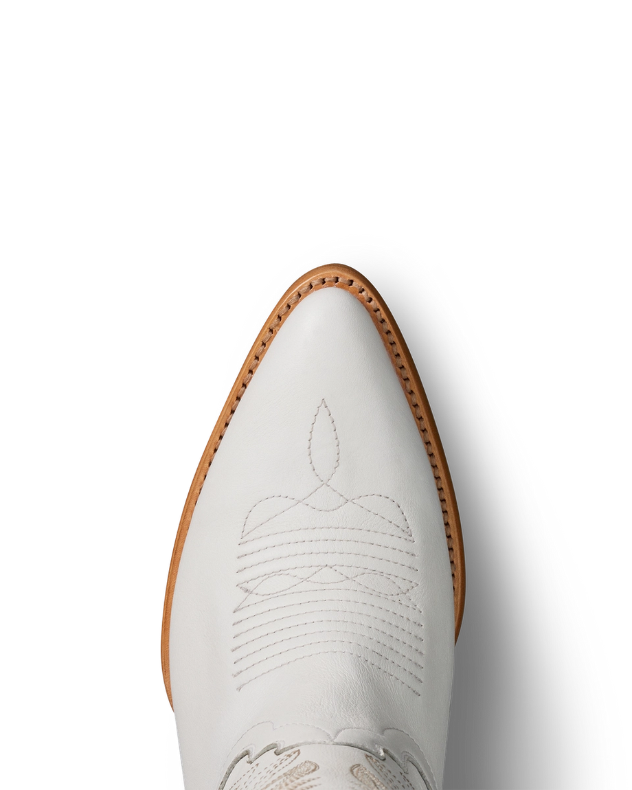 Top view of a white cowboy boot with decorative stitching and a pointed toe, set against a white background with shadow on the right.