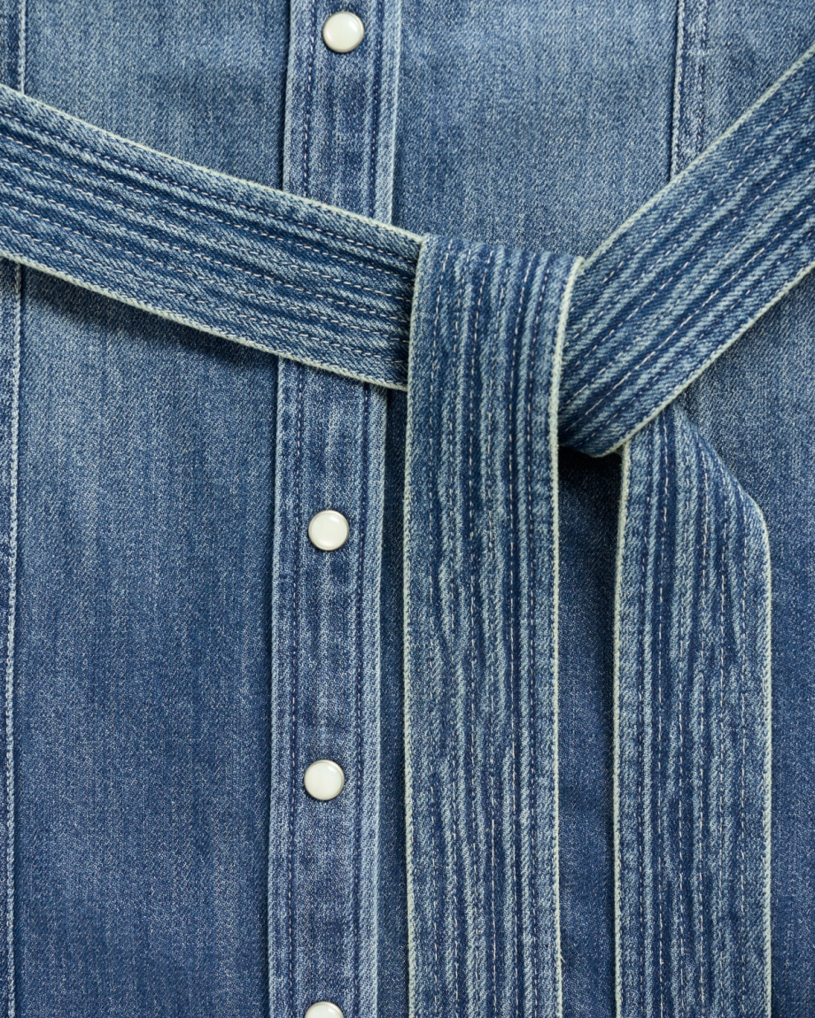 Close-up of a blue denim shirt with a tied waist belt and three white snap buttons.