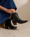 Woman in a denim dress and black booties sitting in a photo studio