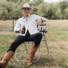 Woman in a cowboy hat, pearl snap shirt, and cowgirl boots drinking a beer in a chair