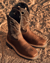 A pair of brown leather cowboy boots with decorative stitching, placed on a dusty surface.